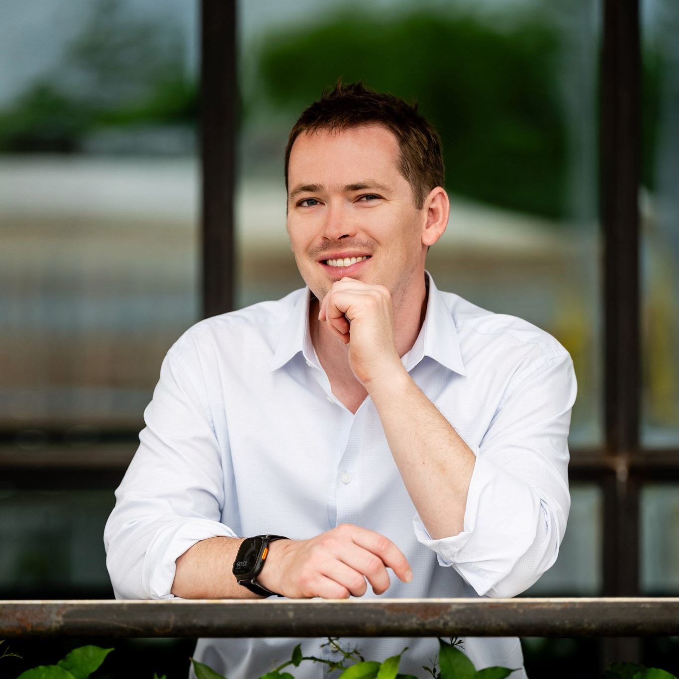 Jon Lofquist smiling over a leafy railing in a white shirt