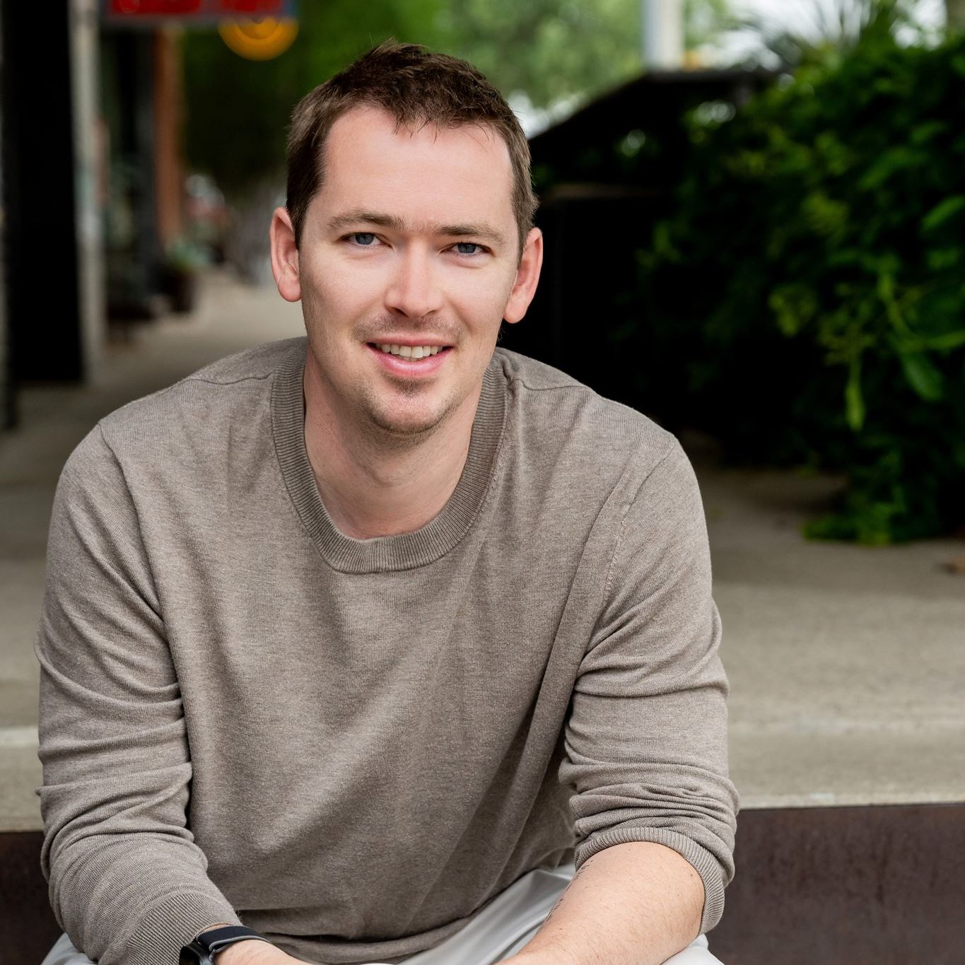 Jon Lofquist sitting on stone steps with a coffee, laughing